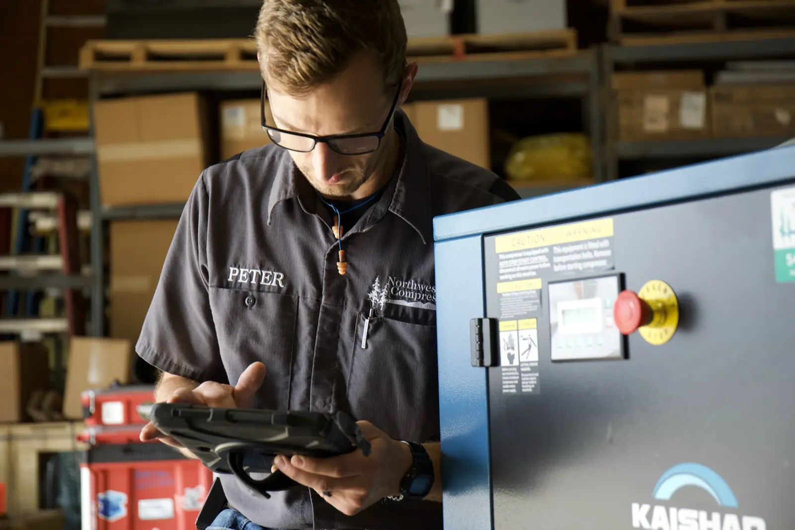 Recording work on a rugged tablet beside a compressor in the shop